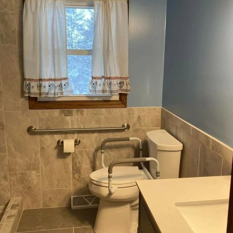 A bathroom with grab bars beside the toilet and along the wall, with a wide vanity top.