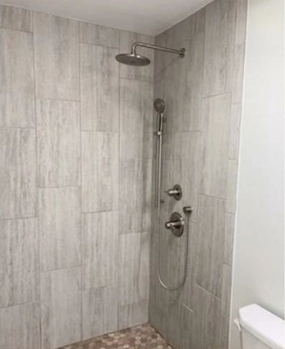 A tiled shower with a rain head, a hand shower and lever trim on a pale tiled wall.