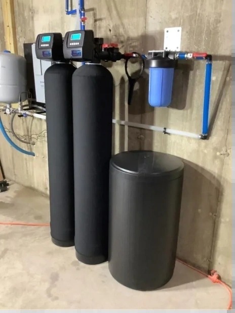 A water treatment set-up against a concrete wall: two tanks with digital control heads, a blue filter housing and a brine tank.