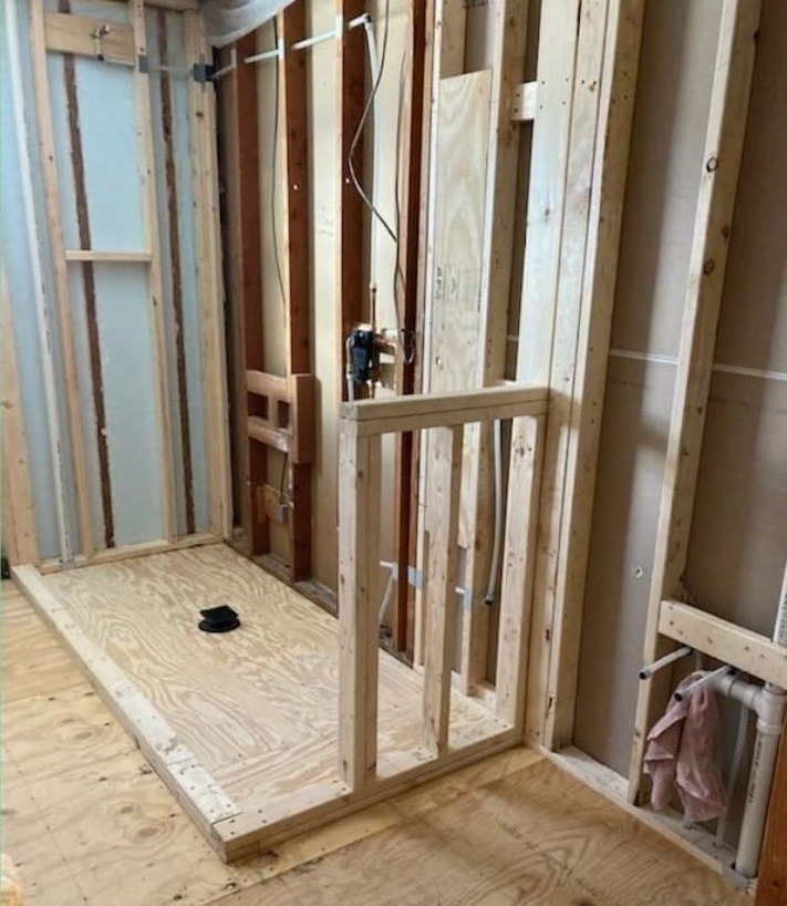 A bathroom opened to the studs with a new shower base framed out and the subfloor exposed.