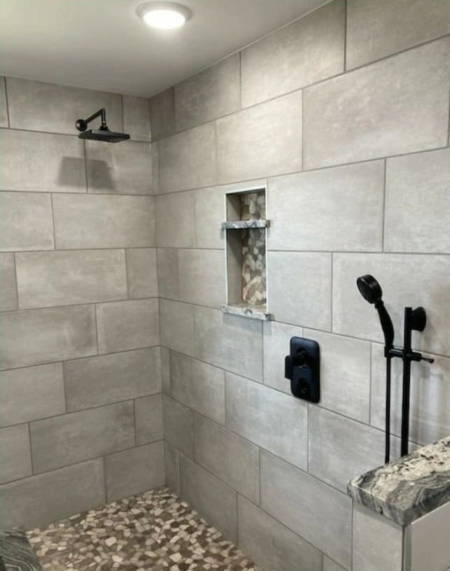 A tiled shower with a recessed niche, a rain head and a hand shower on a slide bar, over a pebble floor.