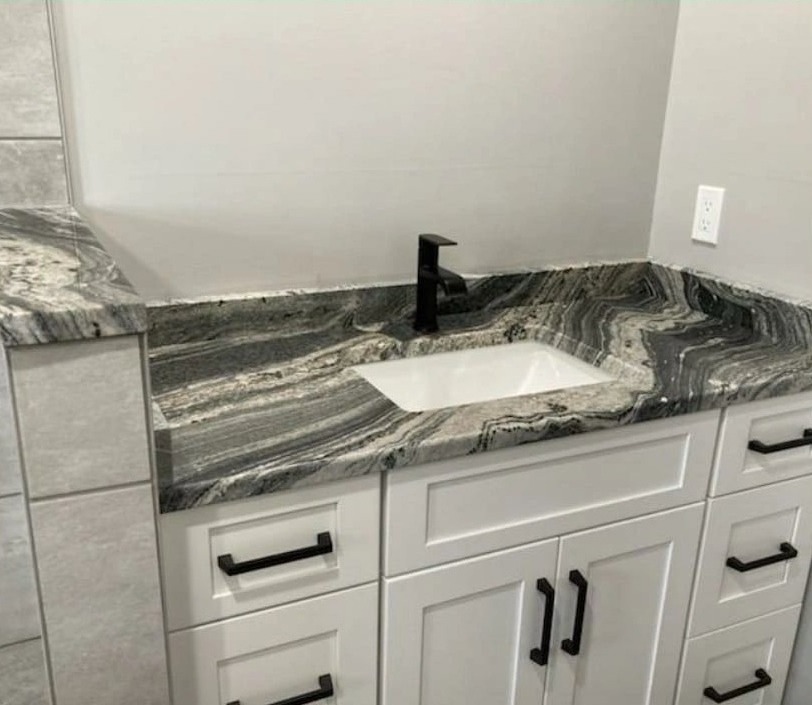 A white vanity with a dark veined stone top, an undermount basin and black tap and handles.